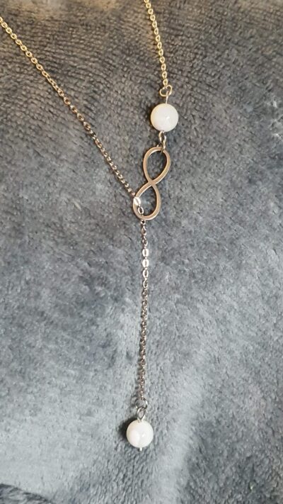 À la recherche d'un pendentif délicat et symbolique pour compléter votre tenue de mariage? Notre pendentif en acier inoxydable hypoallergénique, orné de 2 perles de nacre 8 mm et d'un symbole infini coulissant
